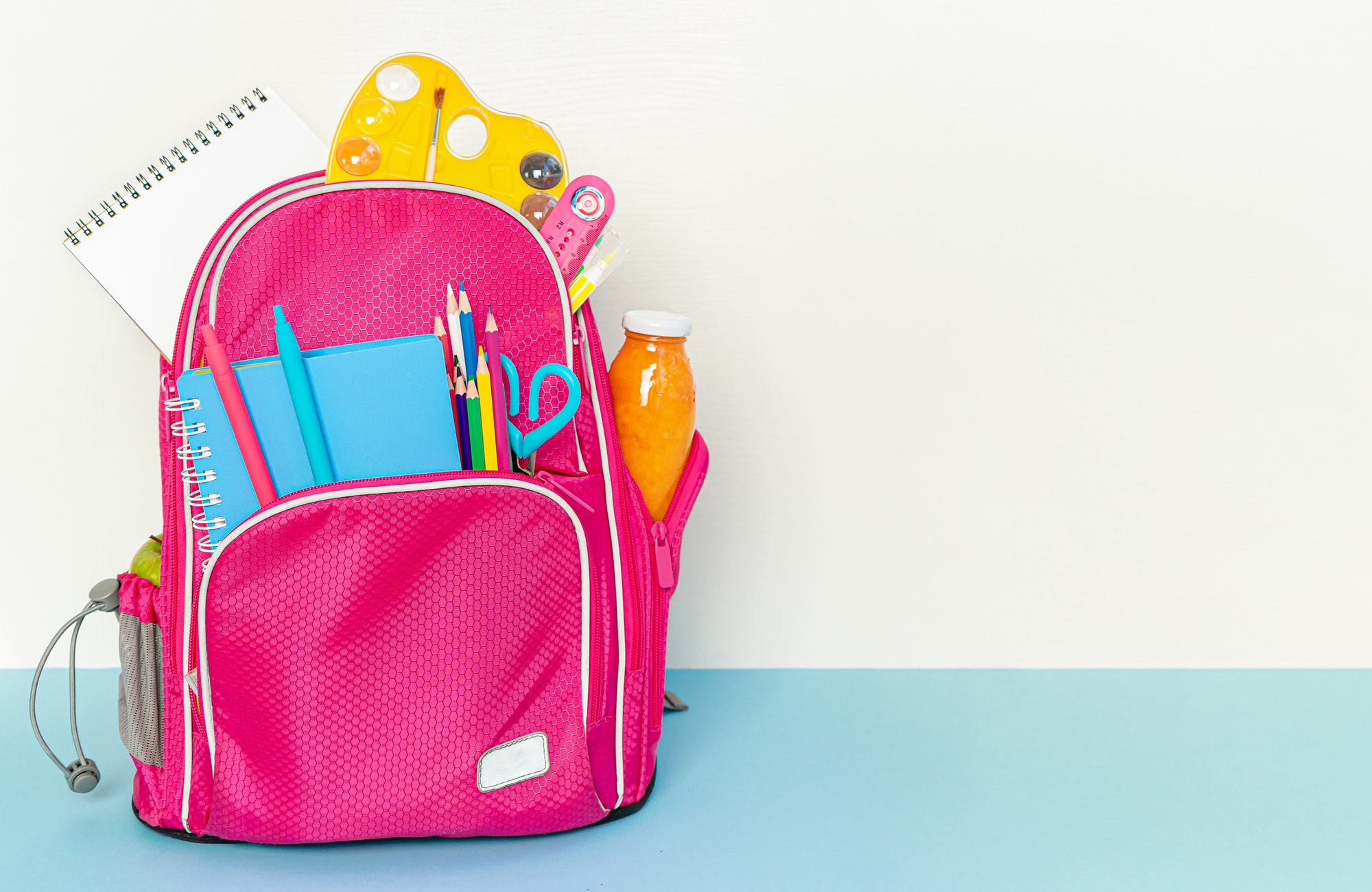 Backpack with school supplies standing on white and blue background. Copy space.